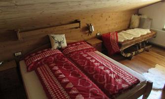 A cozy bedroom with two single beds and rustic wooden paneling. The bedding is red with traditional patterns, and a small wooden stool complements the room.