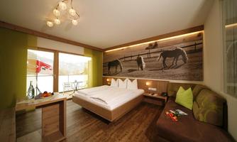 A modern room with a large bed and a beautiful view of nature. The walls are decorated with horse motifs, and there are bright, cheerful colors.