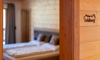 A cozy bedroom with wooden walls and a large bed. On the wall, there is a sign that says "Feldberg."