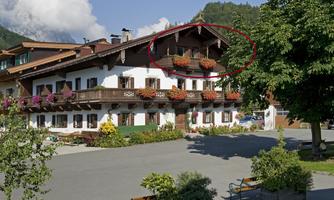 A typical alpine house with balconies full of flowers. In the foreground, there is a square with benches and trees.