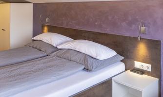 A modern bedroom with a large bed, two pillows, and a minimalist decor. The walls are painted in soft colors and the atmosphere feels inviting.