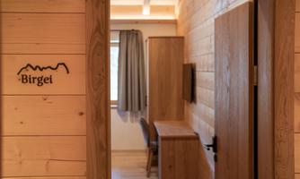 An inviting entrance to a wooden room with a view of furniture and curtains. On the wall, the word "Birgei" is visible in a modern font.