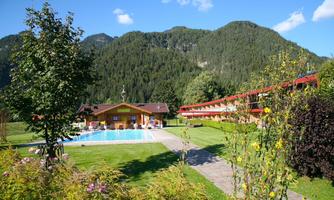 An idyllic holiday home with a pool, surrounded by lush greenery and mountains. The sky is clear and blue, perfect for a relaxing stay.