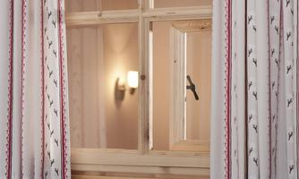 A window with a wooden frame and a delicate curtain. In the background, soft lighting is visible.
