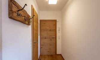 A bright hallway with a wooden hook and wooden doors. The floor is made of light wood and the walls are simply painted white.
