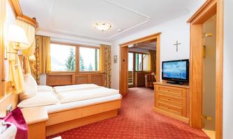 A cozy bedroom with wood paneling and a red carpet. Large windows offer a view of nature.