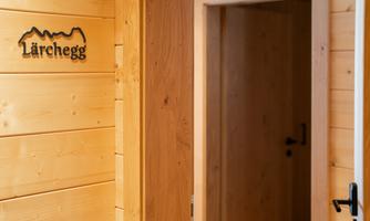 A cozy wooden room with a door leading to another room. A sign adorns the wall with the inscription "Lärchegg."