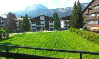 A quiet residential area with green grass and several multi-story buildings. Majestic mountains can be seen in the background.