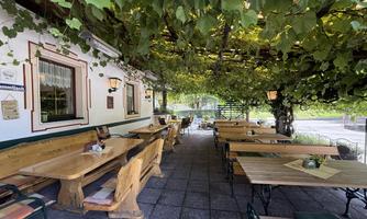A cozy terrace with wooden tables and benches, covered by a green grapevine. The area is bright and inviting, ideal for social gatherings.