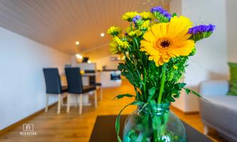 A beautiful bouquet of colorful flowers in a glass vase. In the background, there is a modern living space with a dining area.