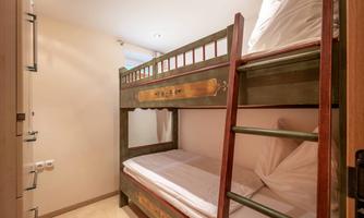A cozy room with a wooden bunk bed and white bedsheets. The walls are light, and the room feels inviting and simple.