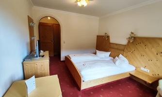 A cozy hotel room with two single beds and wood-paneled furniture. The room has a warm, inviting carpet and a window to the other room.