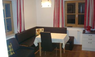 A cozy lounge area with an L-shaped couch and a table. Large windows let in plenty of light, and the walls are painted in light colors.
