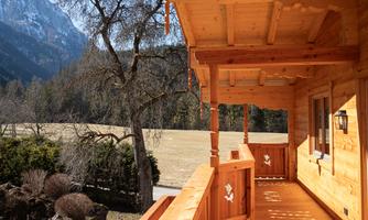 A wooden-clad veranda with a view of a picturesque landscape. In the background, mountains and trees can be seen.