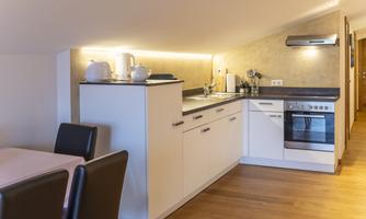 A modern kitchen with bright walls and wooden flooring. It is equipped with a stove, a refrigerator, and a dining area.