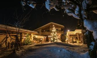 A cozy house in the snow, surrounded by festive Christmas decorations. A illuminated Christmas tree is the centerpiece of the scene.