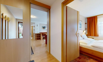 An inviting hallway with wooden interior and a bedroom in the background. The warm colors and natural light create a cozy atmosphere.