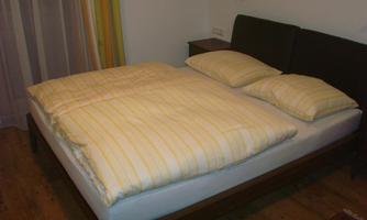 A modern bedroom with a large bed and yellow striped bedding. In the background, curtains and a bedside lamp are visible.