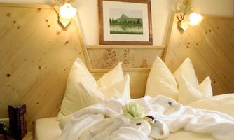 A cozy bedroom with a large bed and many pillows. The walls are made of wood, and a beautiful landscape picture complements the decor.