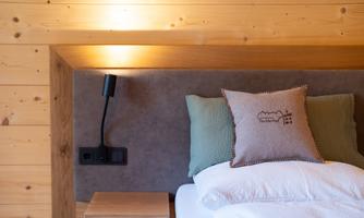 A cozy bedroom with wooden paneling and a stylish headboard. On the bed lies a pillow with a beautiful design.