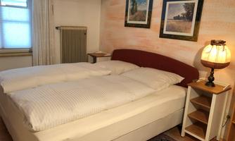 A cozy bedroom with a double bed and a modern lamp. Two pictures hang on the wall, and a window provides natural light.