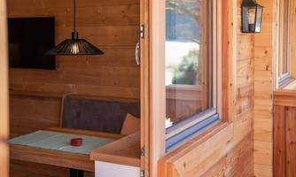 A cozy room with wooden paneling and a table. A hanging lampshade and a window offer a view of the outdoors.