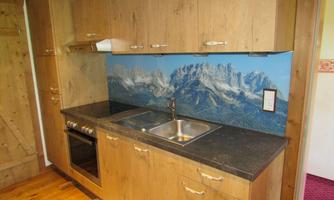 A modern kitchen with wooden cabinets and an attractive countertop. In the background, there is a picture of tall mountains that creates an alpine atmosphere.