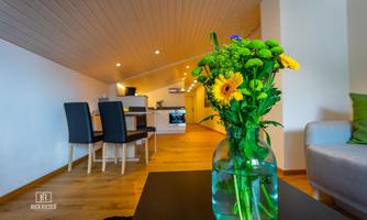 A cozy living kitchen with modern furniture and a beautiful floral arrangement on the table. The bright atmosphere is enhanced by the wood and white tone design.