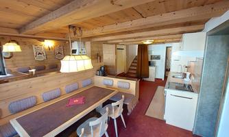 A cozy dining area with wooden paneling and a large table. The kitchen is modern and well-equipped, with access to a staircase.