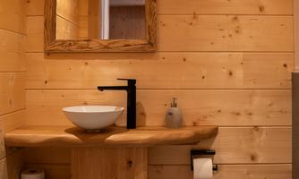 A modern bathroom with wooden cladding. The sink area features an elegant wooden style and a large mirror.