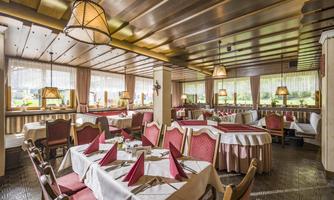 A cozy restaurant with red upholstered chairs and elegant tablecloths. Large windows provide plenty of natural light.
