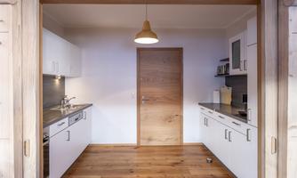 A modern kitchen with bright cabinets and wooden flooring. The door to the kitchen is made of wood and a lamp-shaped light hangs over the room.