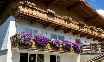 A charming house with flowers on the balconies. The sky is blue and there is plenty of green space all around.