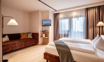 A modern room with a double bed and a cozy sofa. Large windows provide plenty of daylight.