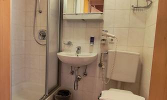 A modern bathroom with a shower, sink, and toilet. The walls are tiled in light colors and the ceiling is made of wood.