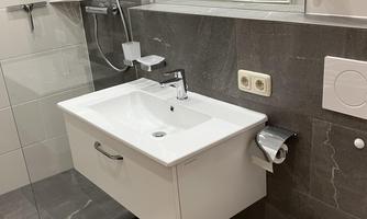 A modern bathroom with an elegant shower and a white sink. The walls are in light shades, and the floor has an appealing design.