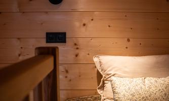 A cozy bedroom with a wood panel wall and a bed. A modern wall lamp gently illuminates over the pillow.