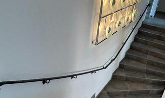 A modern staircase with gray tiles and an elegant railing. A decorative light installation hangs on the wall.