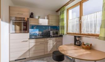 A bright and modern kitchen with wooden cabinets and a beautiful view of the mountains. On the round table, there is a coffee machine and a small basket.
