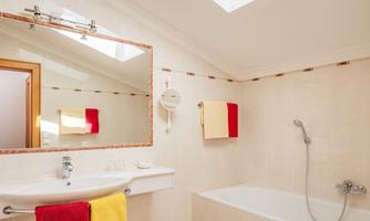 A modern bathroom with a bathtub and a sink. Colorful towels and a large mirror are also visible.