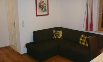 A cozy living room with a dark brown sofa and a colorful cushion. A picture frame hangs on the wall and there is a wooden floor.