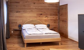 A modern bedroom with wooden paneling and a double bed. The room is bright and cozy.