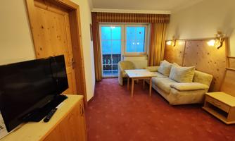 A cozy room with a sofa and a table. The room has a television and a window overlooking a balcony.