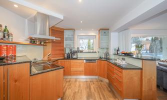 A modern kitchen with wooden cabinets and an elegant countertop. The space is bright and inviting, with large windows and plenty of storage.