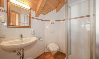 A modern bathroom with a shower and a sink. The walls are tiled white and the ceiling has wooden beams.