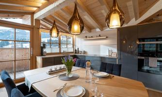 A modern, bright dining room with a wooden ceiling and large windows. The table is elegantly set and illuminated by stylish lamps.