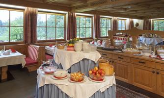 An inviting breakfast buffet with fruits, yogurt, and various baked goods. The rustic decor offers a cozy atmosphere with large windows and a view of the greenery.