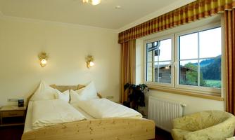 A cozy bedroom with two single beds and a large window. The room is bright and friendly furnished, with a view of the countryside.