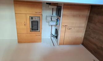 A small kitchen with wooden cabinets and a microwave. It has a sink and a cooking surface.