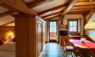 A cozy room with wooden ceilings and furnishings. There is a small table, a television, and a balcony with a view outside.